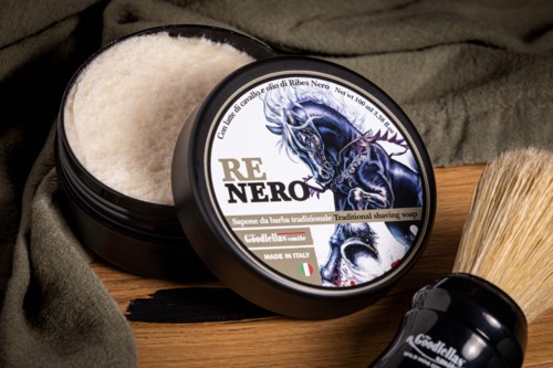 A black container of traditional shaving soap with a dragon image, alongside a shaving brush on a wooden surface.