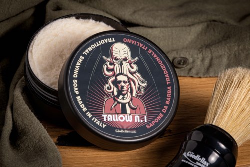 En svart beholder med tradisjonell såpe med en illustrasjon på lokket, ved siden av en barberbørste og noe stoff.