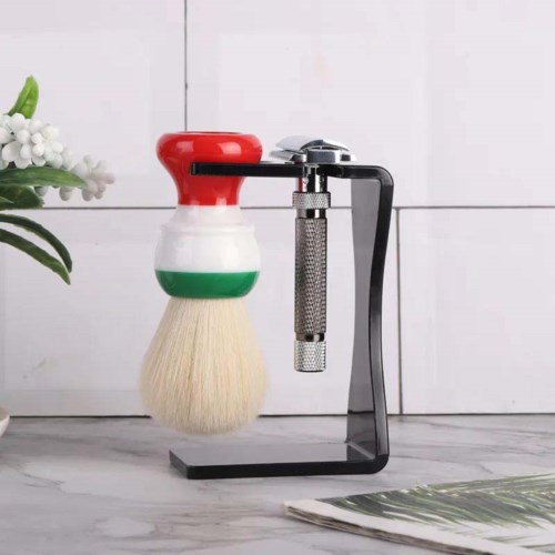 A shaving brush with a handle in red, white, and green colors, mounted on a black stand next to a wall.