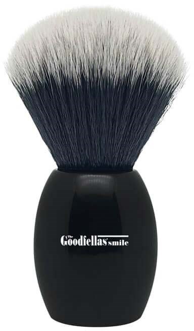 A makeup brush with black handle and soft white and black bristles, labeled 'The Goodfella's Smile.'