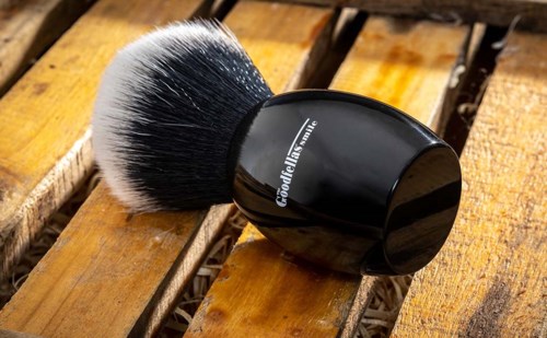 A round black container with a white-and-black makeup brush on a wooden surface.
