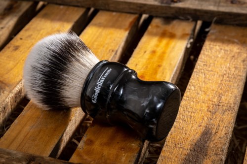 A shaving brush with black handle and white bristles on a wooden surface.