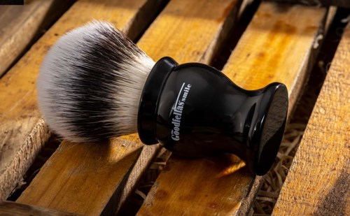 A shaving brush with a black handle and fluffy bristles rests on wooden slats.