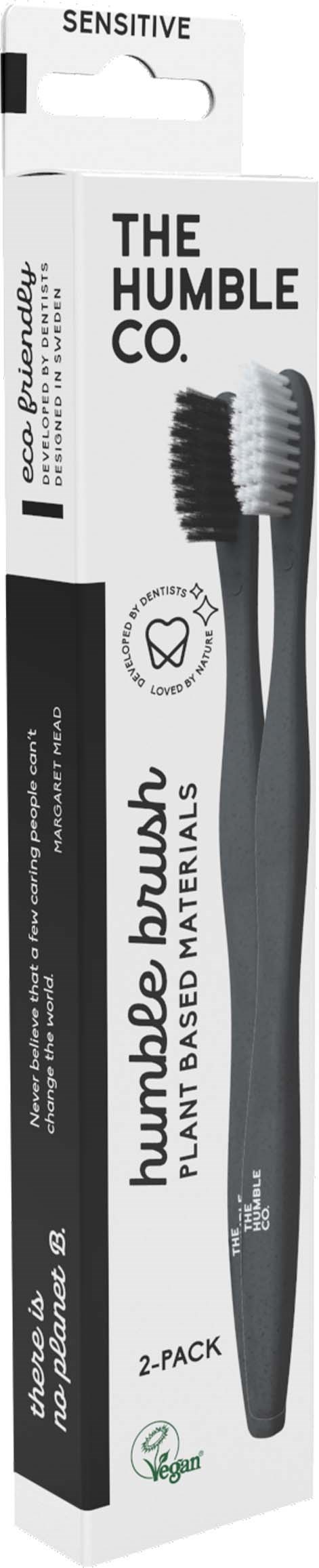 A toothbrush with black and gray handle, labeled for sensitive teeth, in white packaging with black and green text.