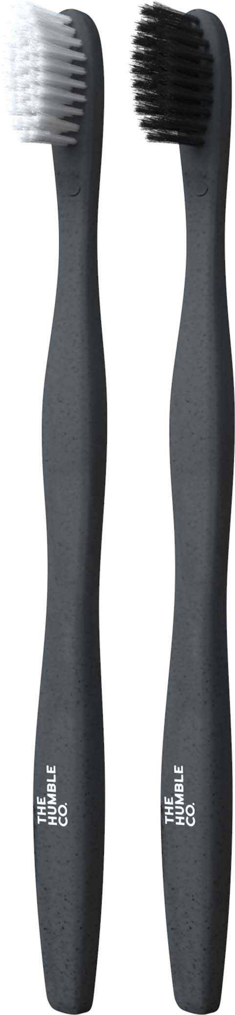 Two toothbrushes, one with white bristles and one with black bristles, stand upright.