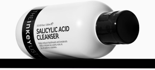 Een witte fles met zwarte dop met label Salicylic Acid Cleanserm, ligt op een zwart-wit achtergrond.