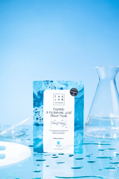 Sininen pakkaus peptide- ja hyaluronihappo-kuidunsuojanaamioille, ympärillä laboratorioskannut ja vesipisaroita.