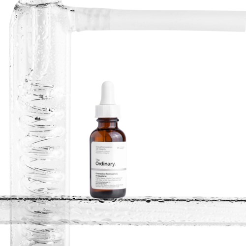Een bruin flesje serum met een witte druppelkraag, geplaatst in een doorzichtige glazen container met water.
