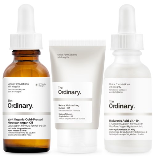 Three skincare products: a dropper bottle, a tube, and a spray bottle, labeled with ingredients and brands, on a white background.