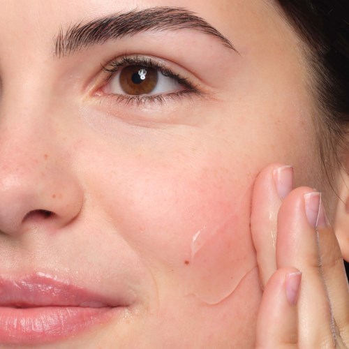 Close-up van een vrouw die haar wang aanraakt, met een heldere huid en natuurlijke make-up.