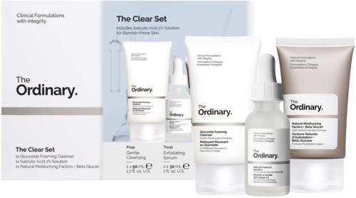En hudpleieserie med rens, peeling, serum, skummende løsning og fuktighetskrem i hvite flasker og tube.