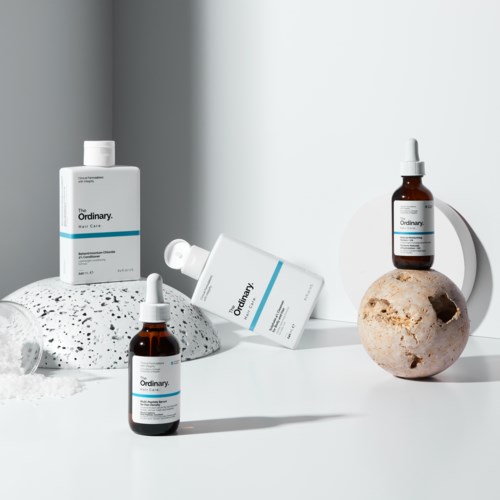 Skincare bottles are placed on a white surface with rocks and a plain background.