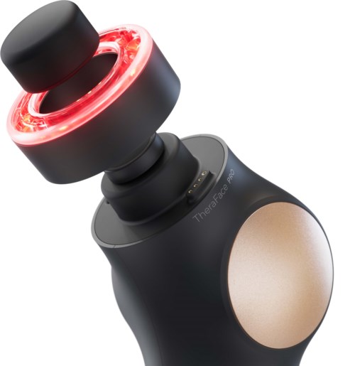 Een zwart apparaat met een rode gloeiende ring en een ronde massagkop, gelabeld Theraface Pro voor gezichtsbehandeling.