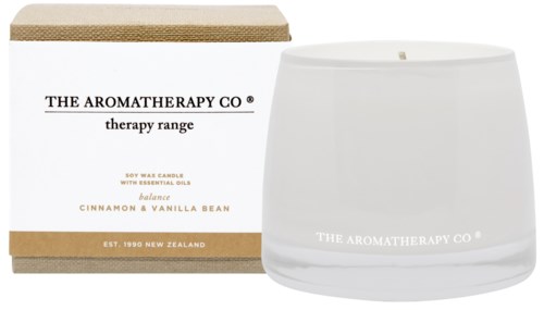 A white candle in a glass jar with label and a box next to it, both have the brand name 'The Aromatherapy Co.' and scent details.