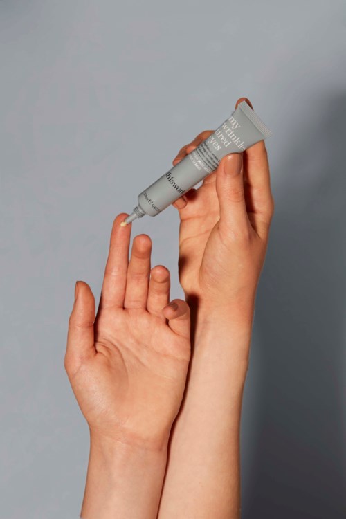 Een persoon brengt crème of verf aan op hun vinger met een tube, met een neutrale achtergrond.