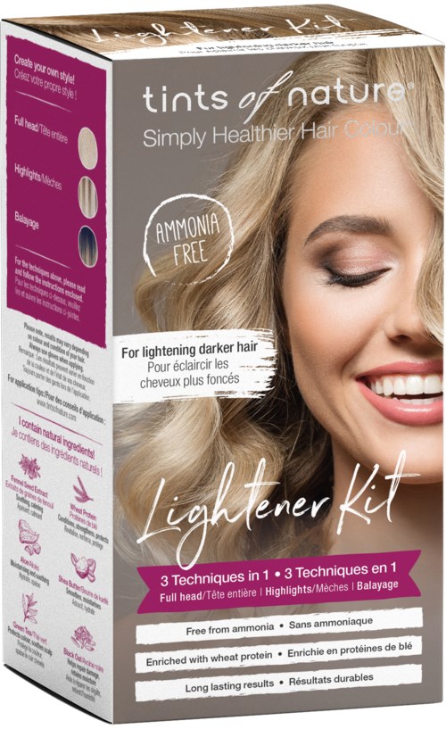 A woman with blonde hair smiling, holding a hair dye product box that highlights lightening darker hair and is ammonia free.