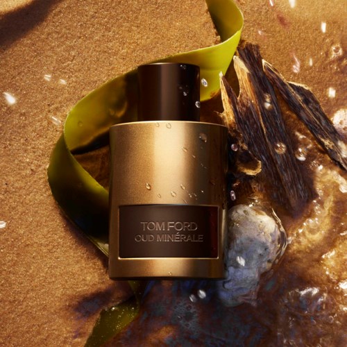 Een fles Tom Ford Oud Minérale-parfum omringd door stenen, zeewier en bubbels, waardoor een luxe en natuurlijke scène ontstaat.