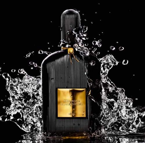 Een zwarte parfumfles met gouden label spat in water tegen een donkere achtergrond.
