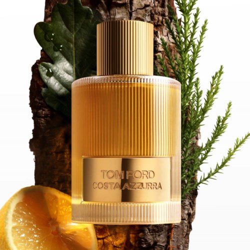 Een parfumfles met de naam Tom Ford Costa Azzurra, geplaatst op een boomstam met bladeren en een sinaasappelschijf ernaast.