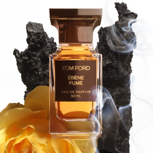A perfume bottle labeled 'Tom Ford Ébène Fumé' surrounded by black volcanic rocks and yellow flower petals.