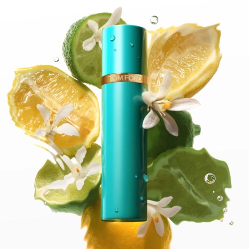 A turquoise perfume bottle surrounded by lemon, lime, and white flowers with water drops.