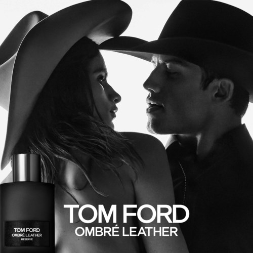 Svartvit bild av en man och kvinna som möts, bär hattar, med Tom Ford Ombré Leather parfymflaska synlig.