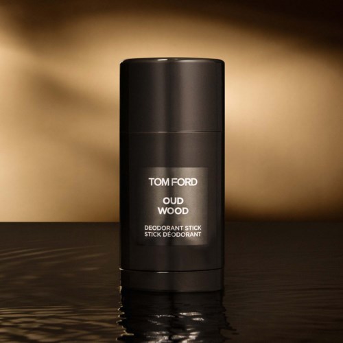 A black deodorant stick container with white text for Tom Ford Oud Wood on a dark reflective surface.
