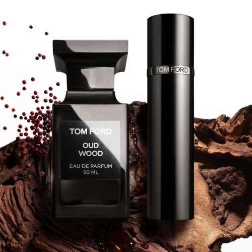 A perfume bottle labeled 'Oud Wood' with scattered red peppercorns and textured brown background.