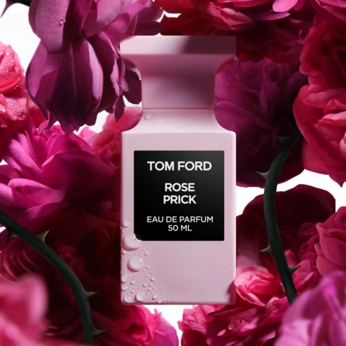 A white perfume bottle surrounded by pink and red flowers, with text on the bottle labeling it as Tom Ford Rose Prick.