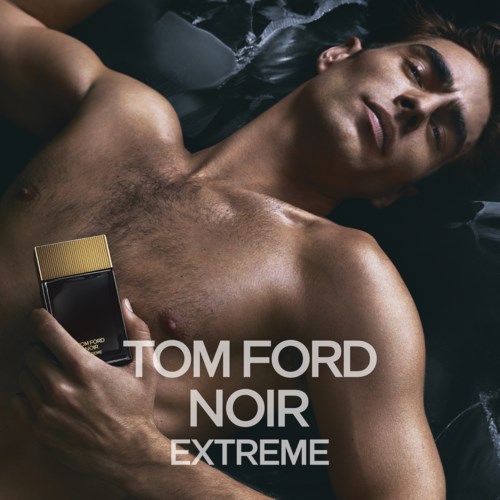 Enbart överkropp hela mannen ligger på svarta lakan, håller en parfymflaska, med text om Tom Ford Noir Extreme.