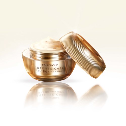 A gold-colored jar of Tony Moly skincare cream with its lid slightly open, cream visible inside, on a reflective surface.