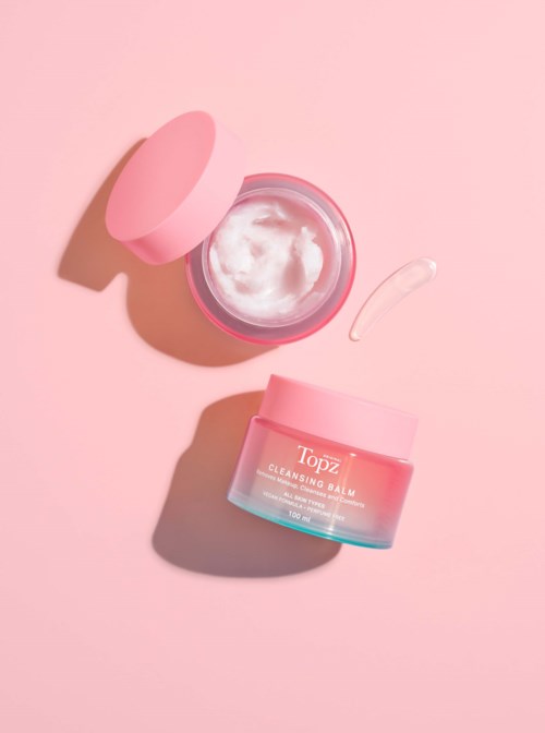 Pink container of cleansing balm with a small spatula on a pink background.