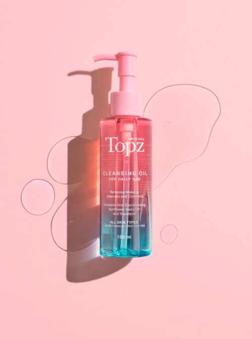 A pink and blue cleansing oil bottle with a pump on a pink background, with some floaty circles nearby.