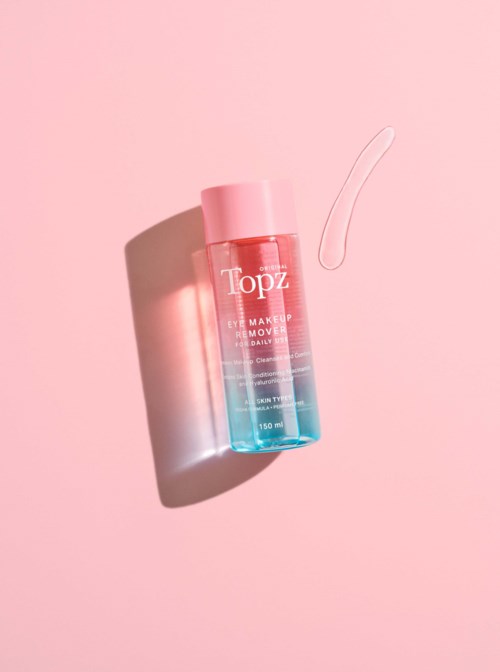 A pink and blue bottle of makeup remover with a piece of cream or gel next to it on a pink background.