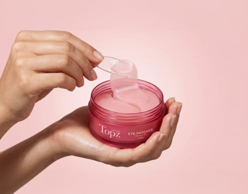 Hands holding a pink jar of eye patches, with a small spatula lifting one patch out.
