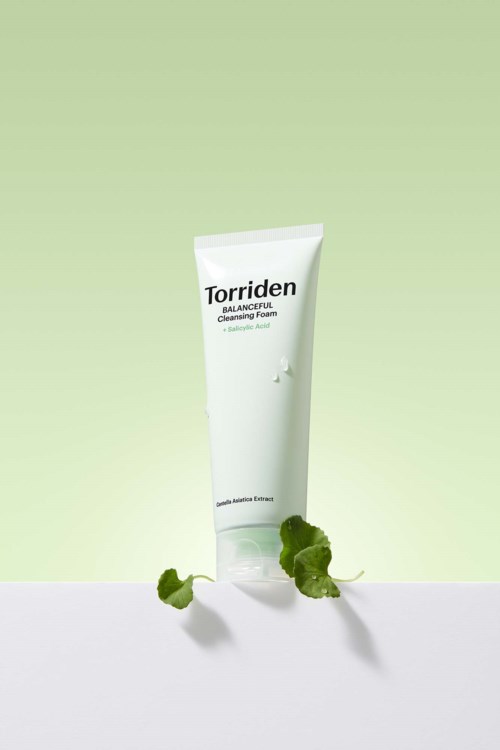 A white tube of Torriden face cleanser with a green background and small green leaves nearby.