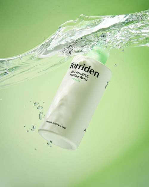 A white bottle with green cap is falling into water, creating splashes and bubbles. Background is light green.