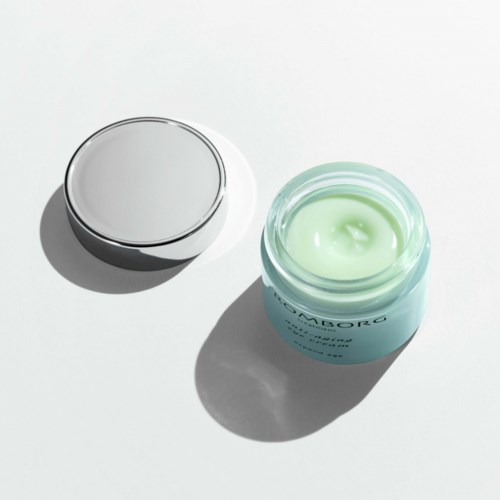 Offener Behälter mit hellgrüner Creme und silberner Deckel auf weißer Oberfläche, Schatten.