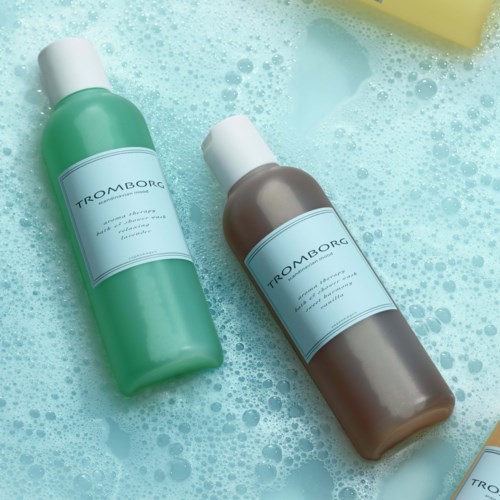 Zwei Flaschen Shampoo oder Duschgel liegen auf schäumendem Badewasser.