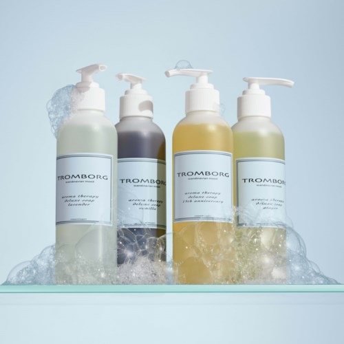 Vier Flaschen mit Pumpen, beschriftet 'Tromborg', enthalten Seife oder Lotion, in einer Reihe mit Schaum und Blasen.