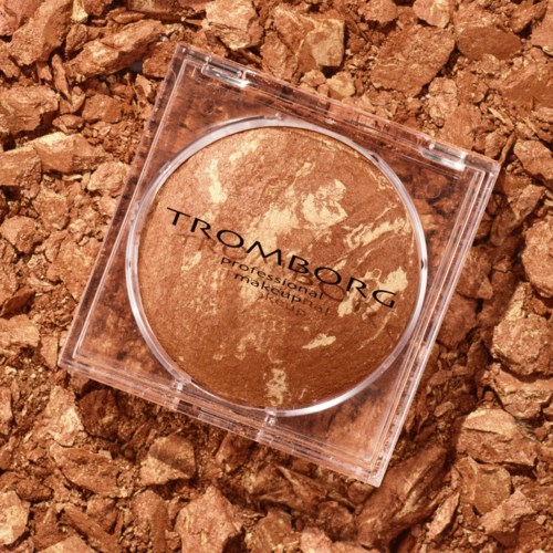 A round, shimmery bronzer compact on a textured, brown background.