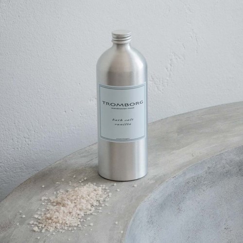 Eine silberne Flasche mit dem Label 'Tromborg bath salt vanilla' steht auf einer grauen Oberfläche, daneben Salz verstreut.