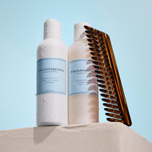 Two white bottles with blue labels and a brown comb rest on a surface against a blue background.