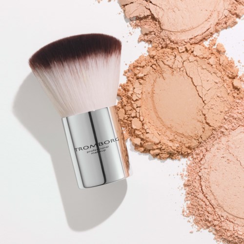 A makeup brush with powder spilled next to it on a white surface.
