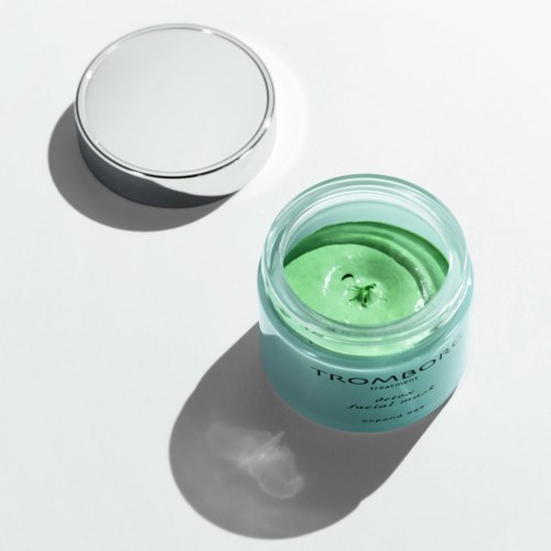 Ein Behälter mit grüner Creme oder Gel, mit einem silbernen Deckel daneben auf einer weißen Fläche.
