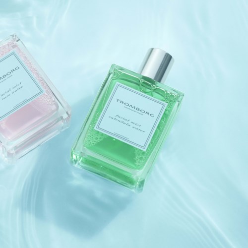 Zwei Parfümflaschen, eine grün und eine rosa, liegen auf einer glänzenden Oberfläche. Die grüne Flasche ist auffällig und klar.