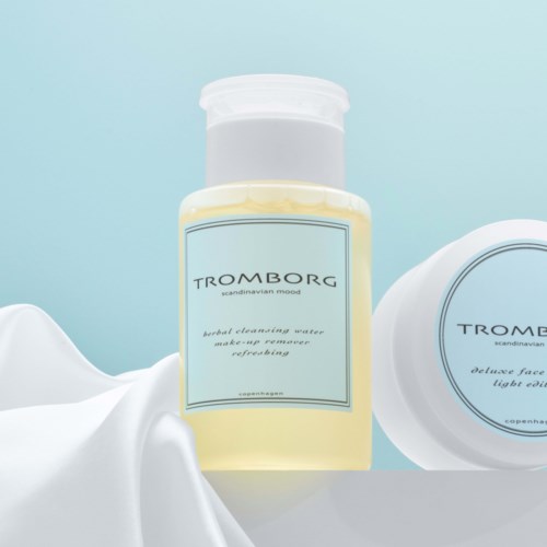 A bottle of TROMBORG skincare product with a light blue label, beside a round container and white fabric.