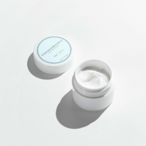 Ein kleines rundes Behältnis mit Creme oder Lotion neben einem weißen Hintergrund.