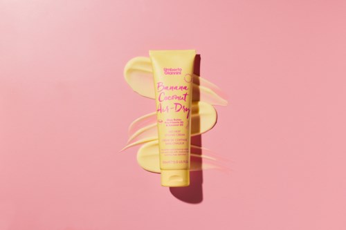Ein gelber Tuben Hautpflegecreme mit pinkem Text, auf einem pinken Hintergrund mit einer cremigen Spirale darum.