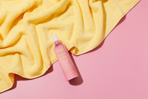 Pink spray bottle with yellow towel on pink background.